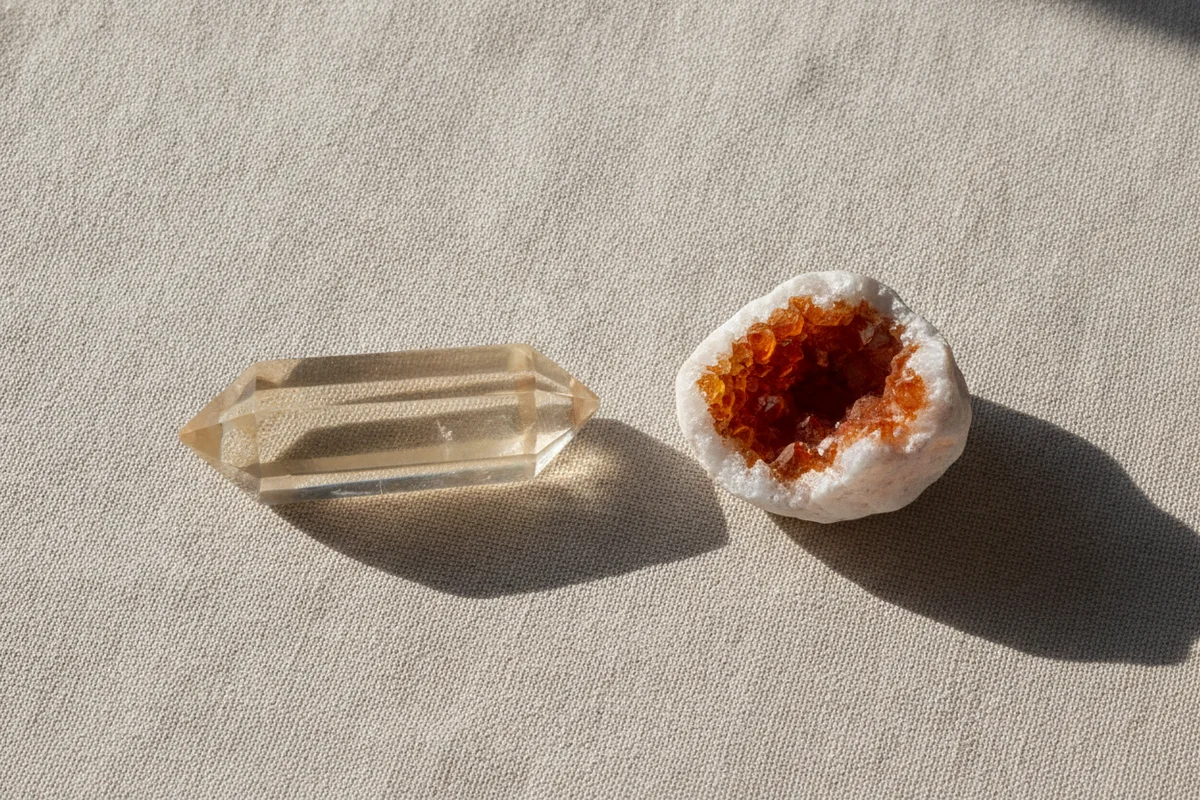 Citrine : une pointe de citrine naturelle jaune pâle posée à côté d’une petite géode orange à la base blanche, sur un tissu de lin clair